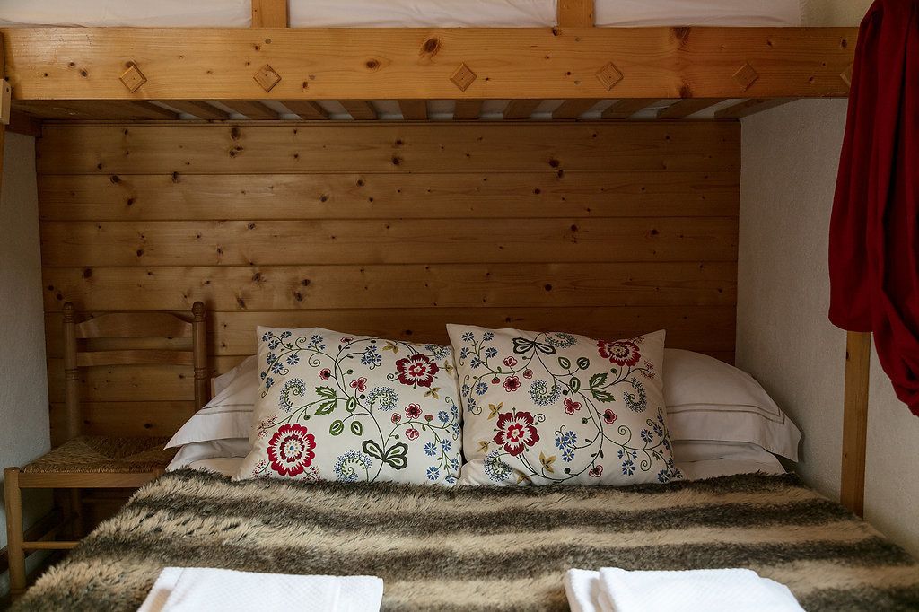 Un letto a castello in legno con cuscini a motivi floreali e una coperta a righe.