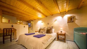 A cozy bedroom with a wooden ceiling, a bed with a beige blanket, a nightstand with a lamp, and a small desk with a chair. - Chilly Powder - Hôtel au Coin du Feu (Morzine)