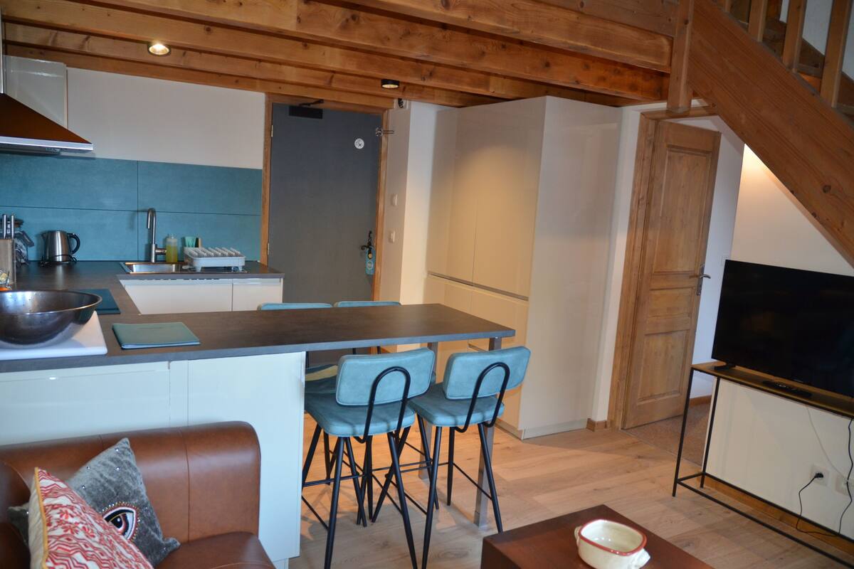 A compact kitchen with a dining area, wooden ceiling, and a TV in a corner.
