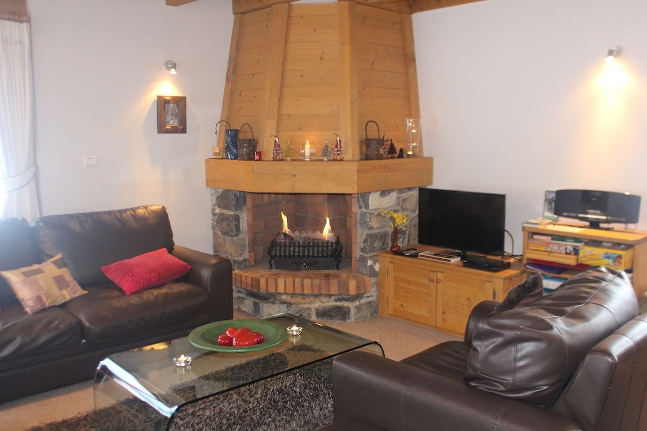A living room with a stone fireplace, leather sofas, a glass coffee table, and a television.