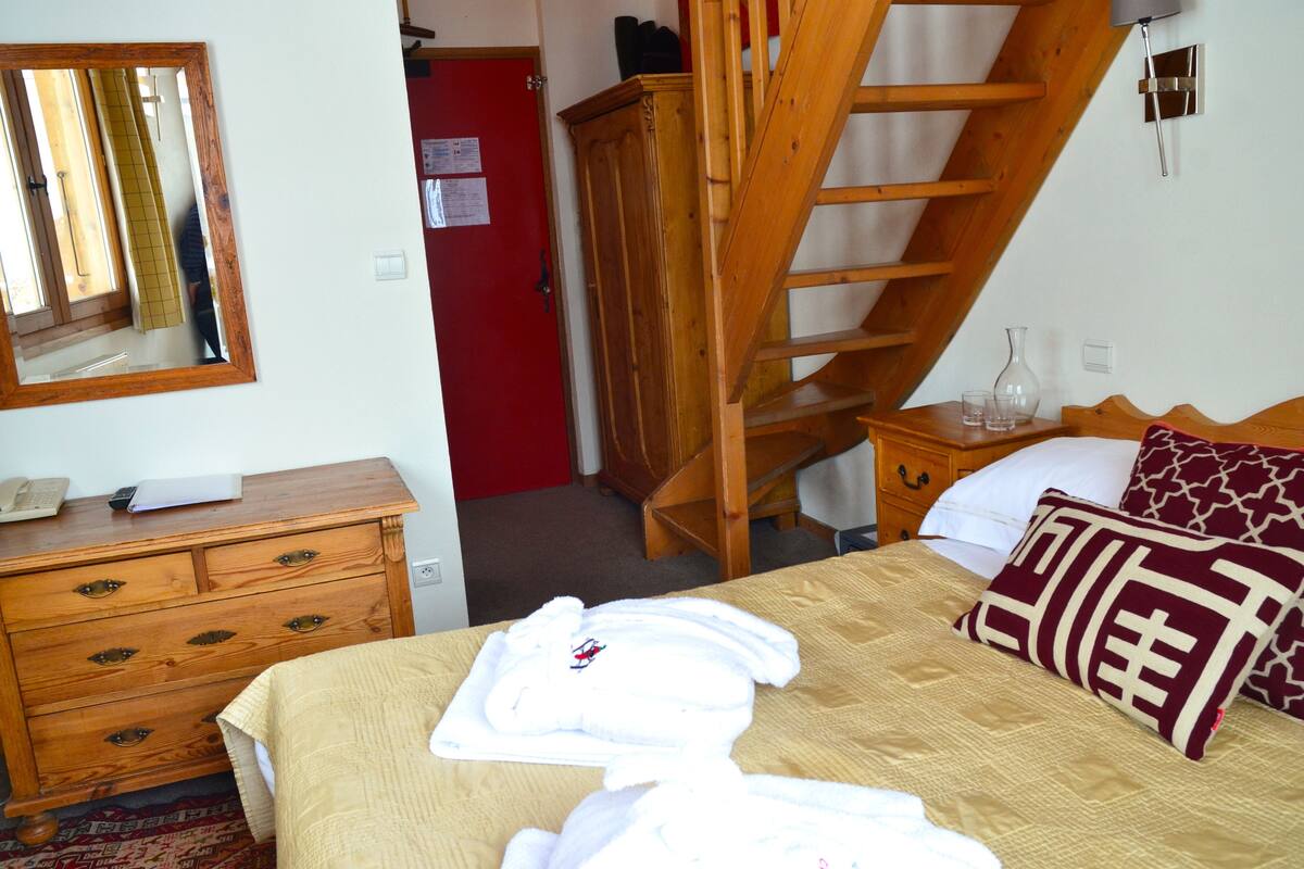 A bedroom with a wooden dresser, a bed with a beige comforter, and a wooden staircase.