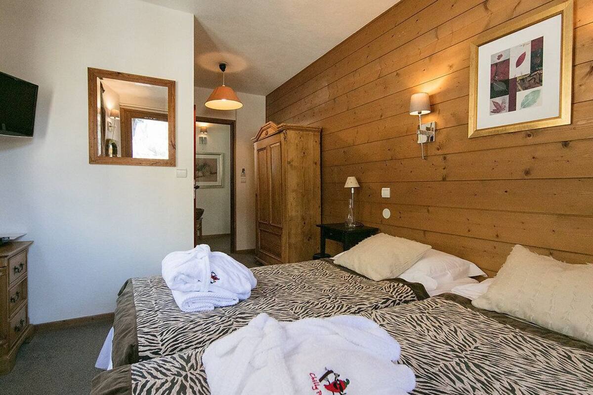 A hotel room with two beds, wooden paneling, a mirror, a television, and a framed picture on the wall.