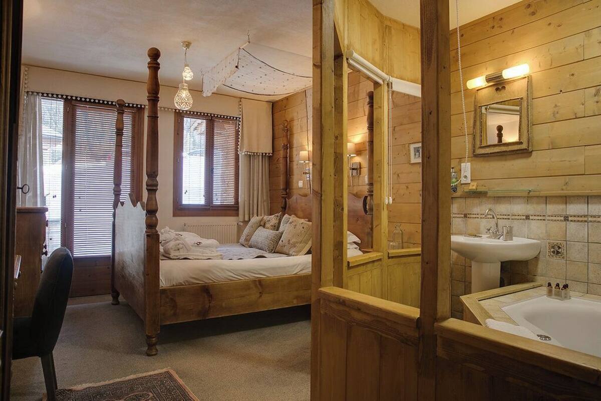 A bedroom with a wooden bed, a chair, and a window with blinds.