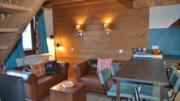 Un intérieur chaleureux en bois, avec un canapé, des fauteuils, une table à manger et un coin cuisine.