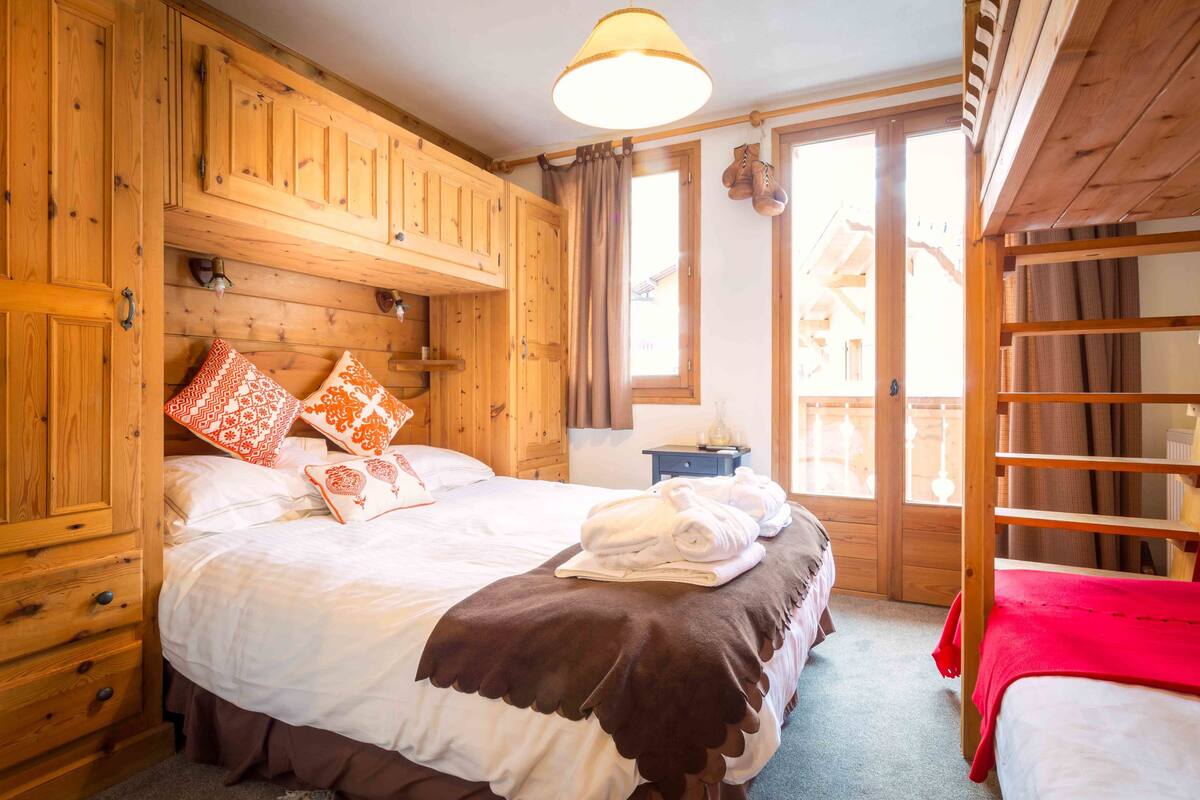 A wooden room with a bed, a nightstand, and a window with curtains.
