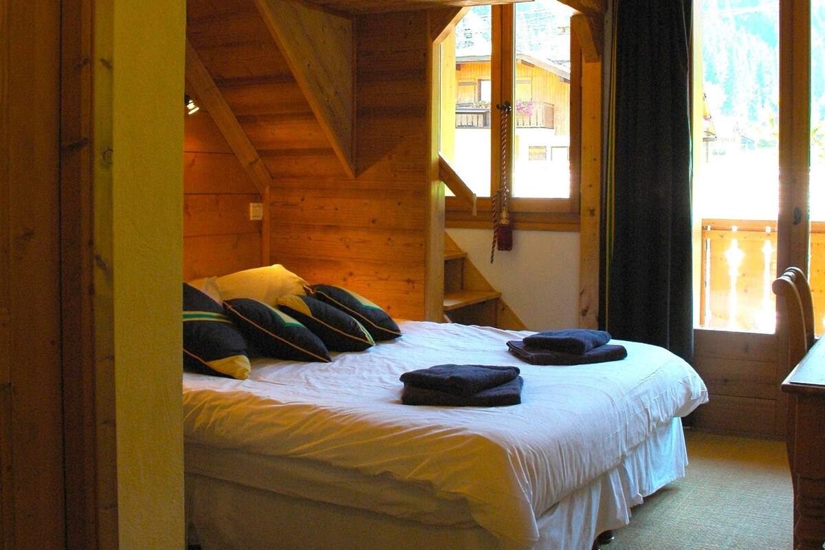A wooden cabin bedroom with a bed, pillows, and a window with curtains.