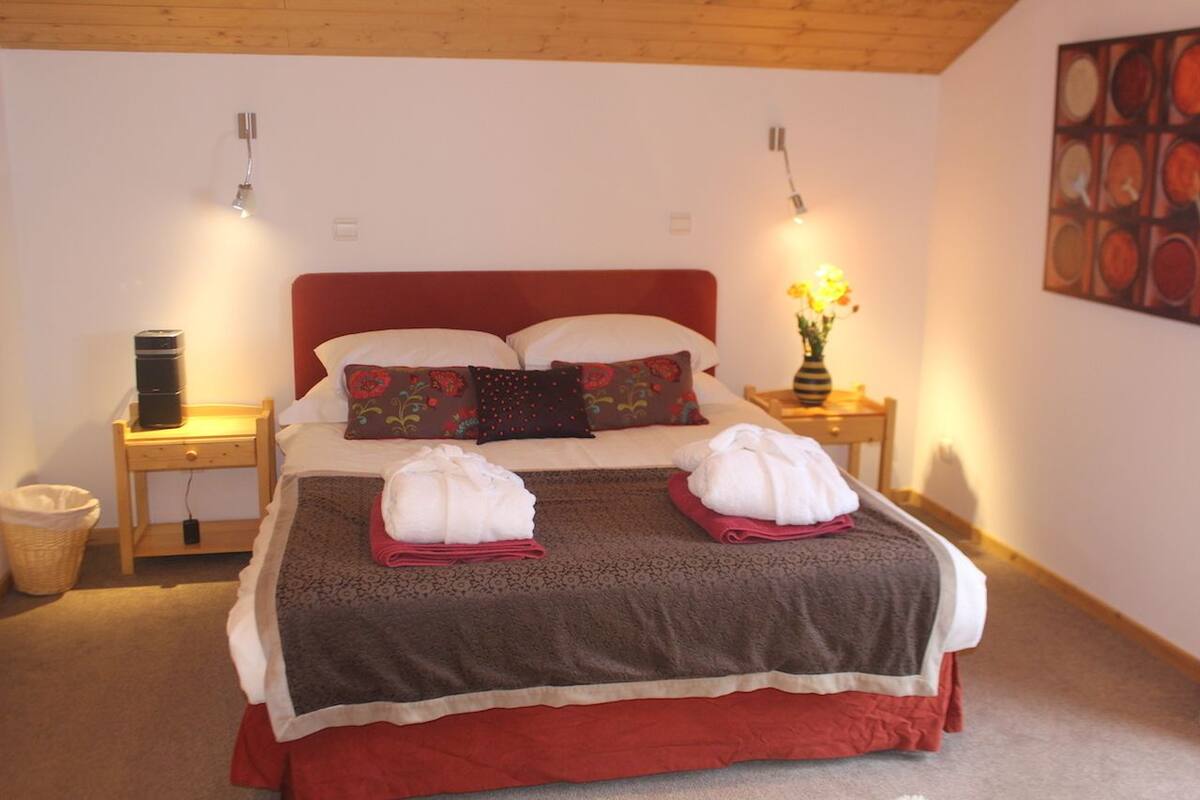 A neatly made bed with two towels, a red headboard, and a wall-mounted lamp.
