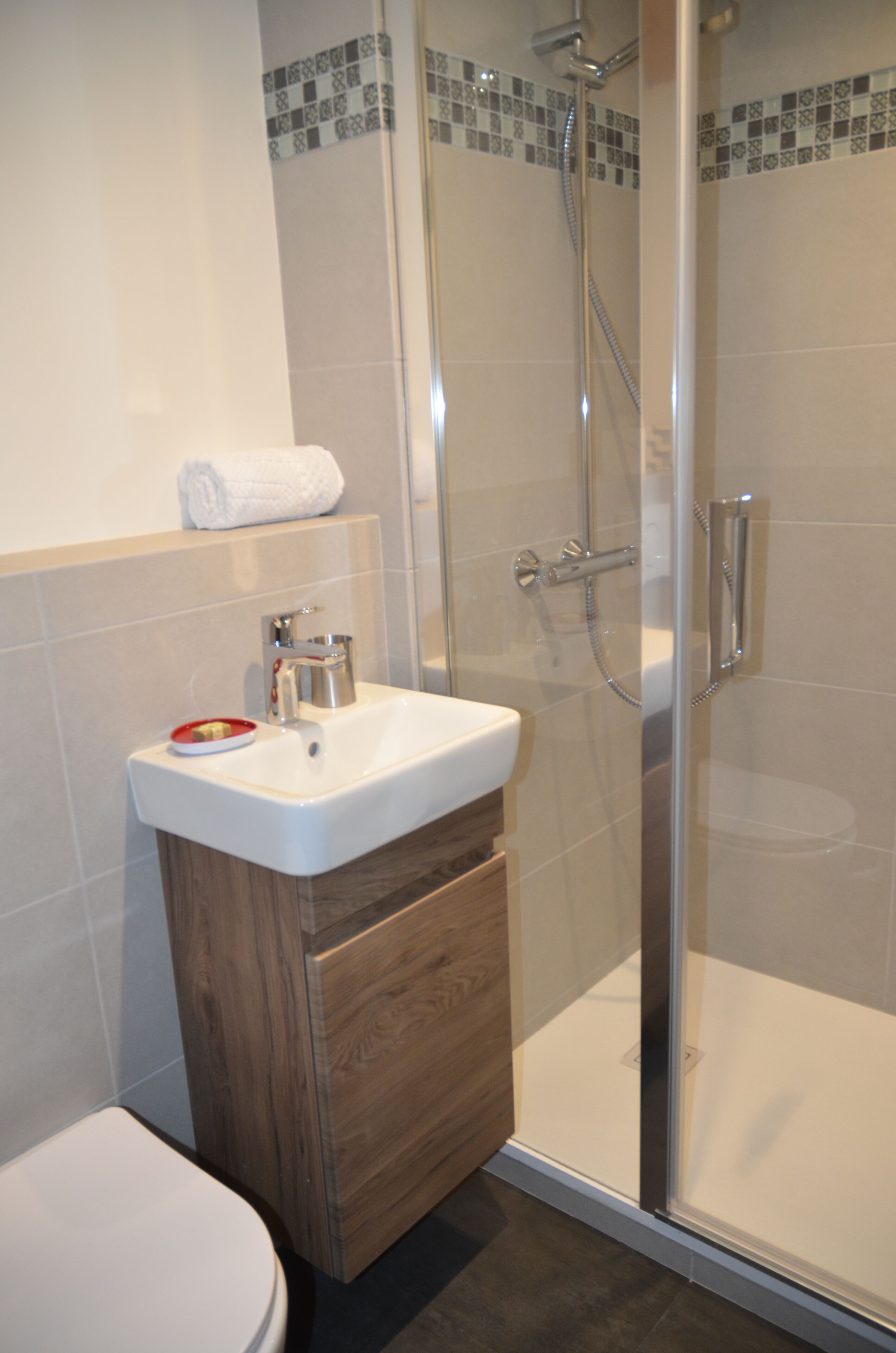 A bathroom with a glass-enclosed shower, a white sink with a wooden cabinet, and a white toilet.