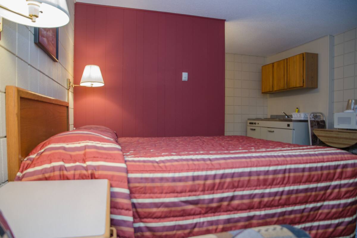 Una habitación con cama, escritorio, lámpara, microondas y un armario.