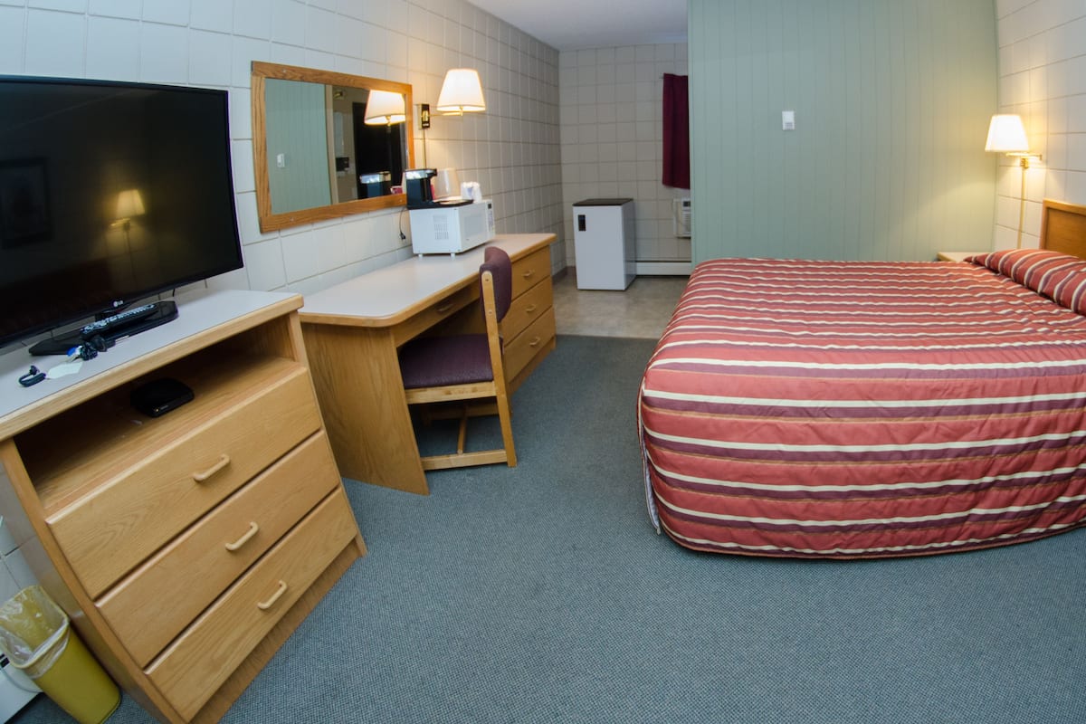 Una habitación de hotel con cama, escritorio, televisor, espejo y lámpara.