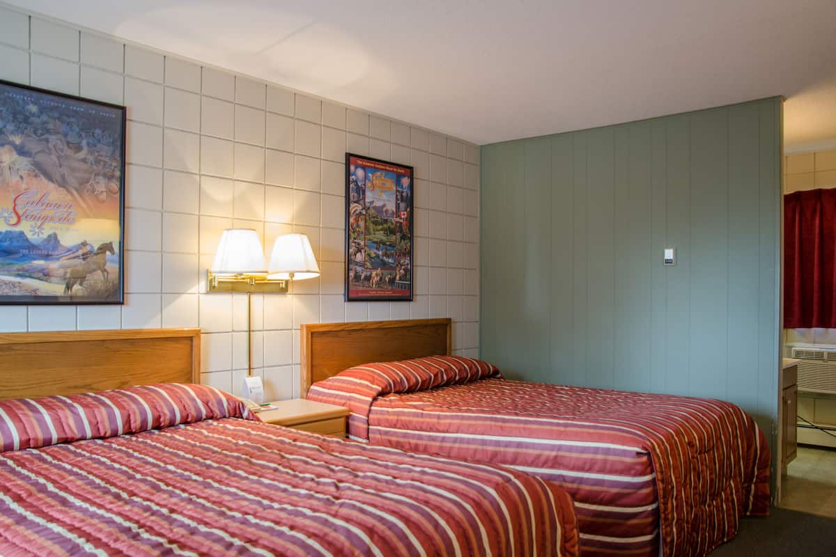 Habitación de hotel con dos camas, una mesita de noche, una lámpara y dos cuadros en la pared.