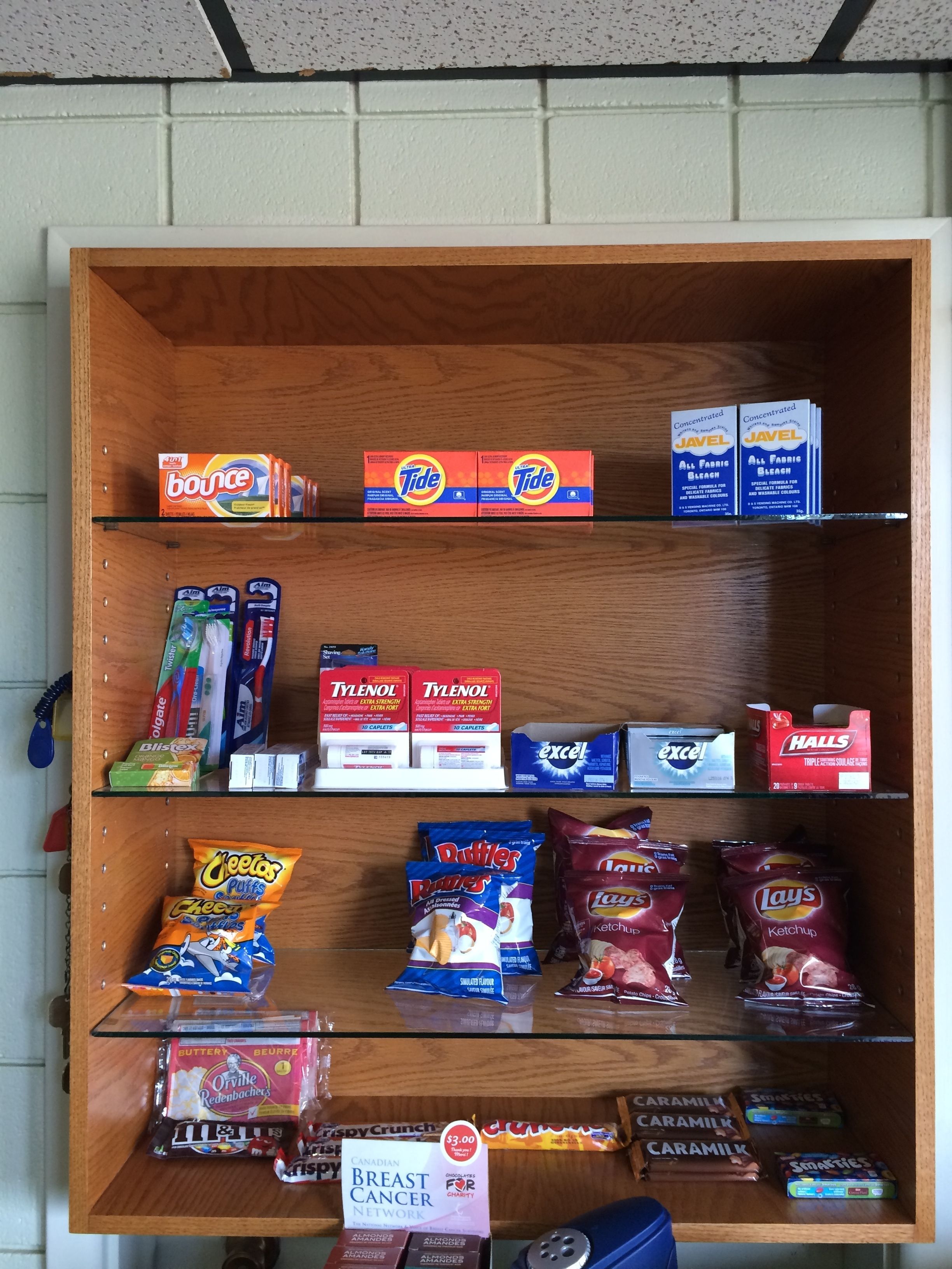 A shelf stocked with various grocery items including Tide detergent, Tylenol, and snacks like Lay's chips.