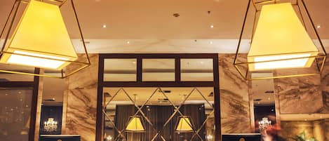 A lobby with marble walls, two large geometric chandeliers, and a reflective glass partition.