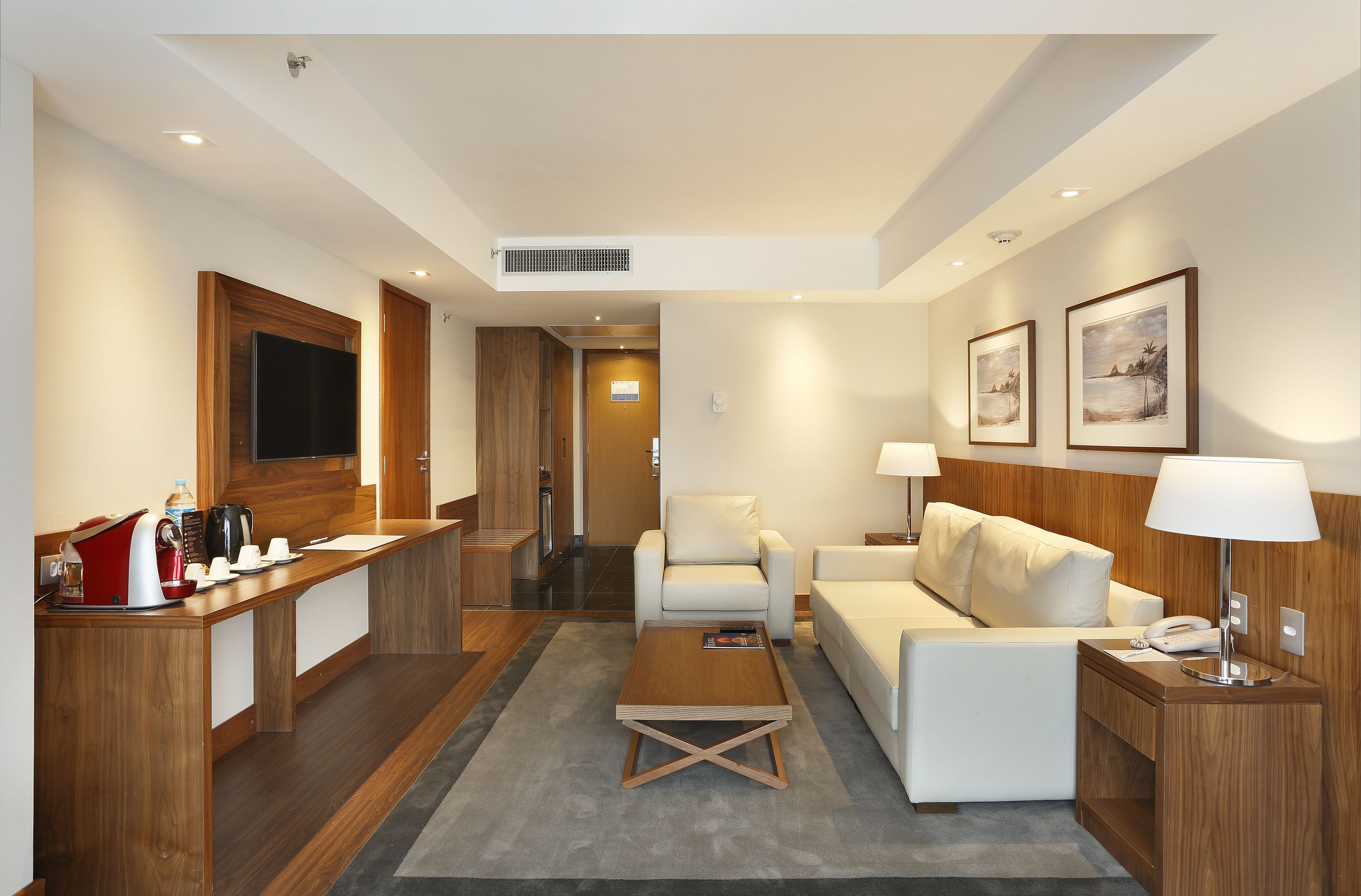 Une chambre d’hôtel avec un bureau en bois, un canapé, une table basse, une télévision et un lit.