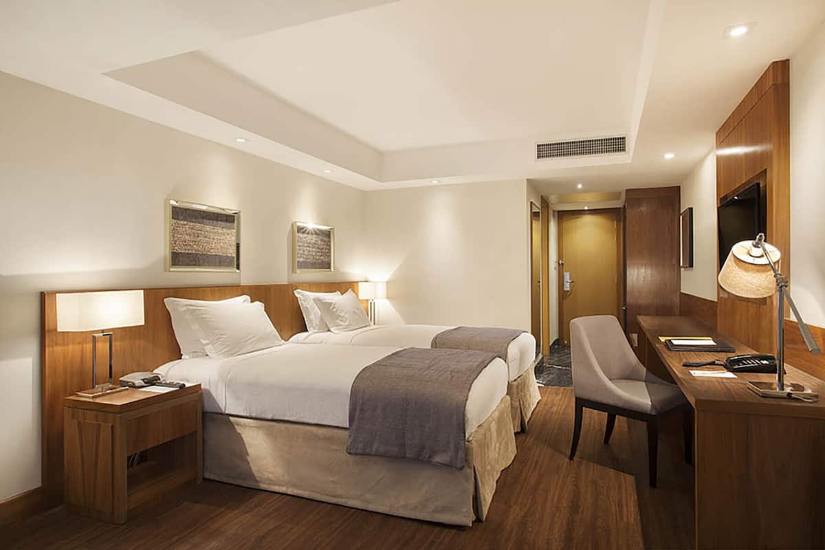 Ett hotellrum med två sängar, ett skrivbord, en stol, en lampa och en tv.