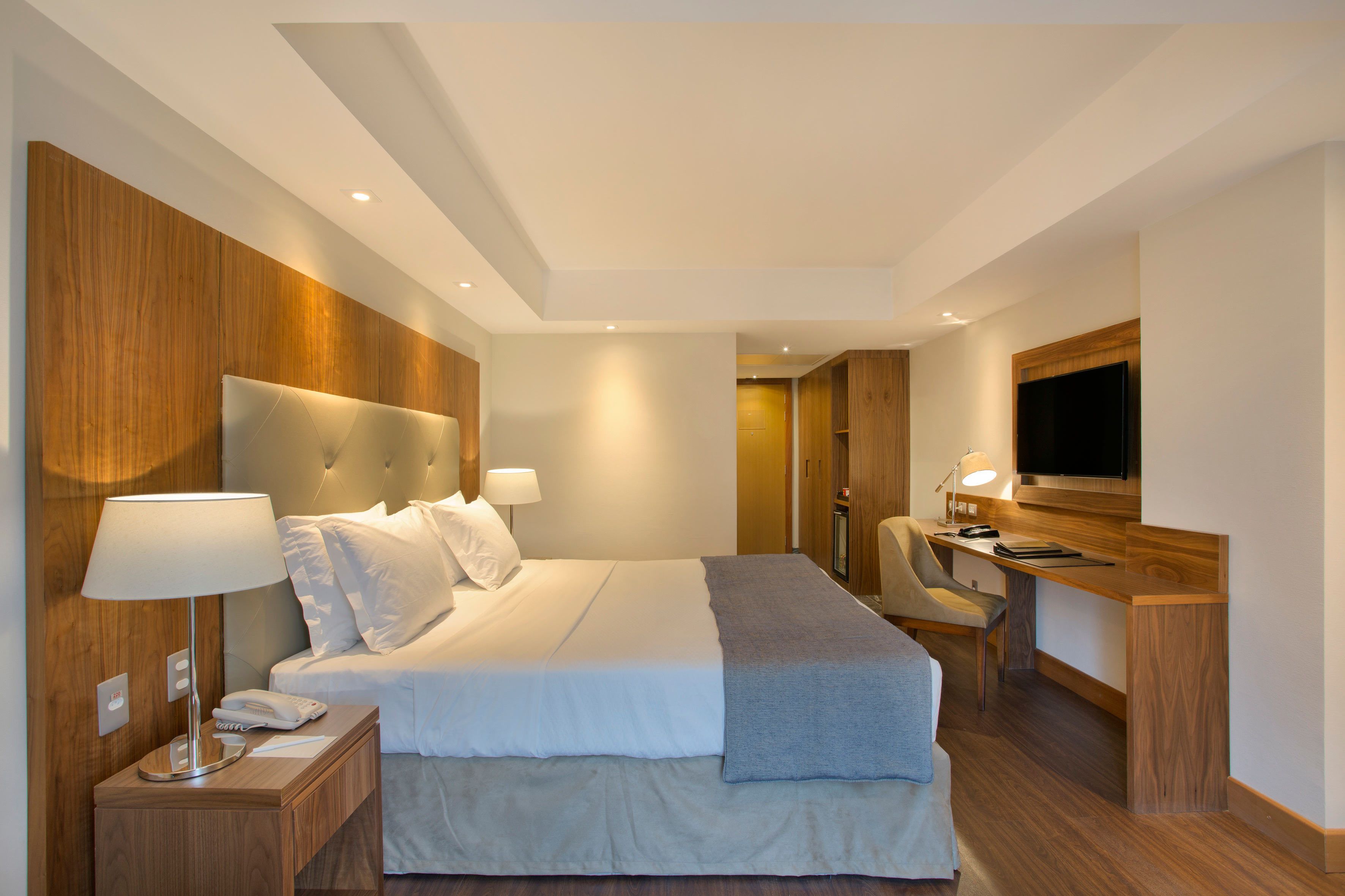 A modern hotel room with a large bed, bedside lamps, a desk with a chair, and a flat-screen TV.