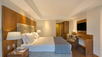 A modern hotel room with a large bed, bedside lamps, a desk with a chair, and a flat-screen TV.