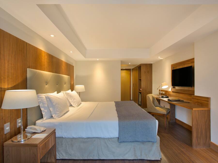 A modern hotel room with a large bed, bedside lamps, a desk with a chair, and a flat-screen TV.