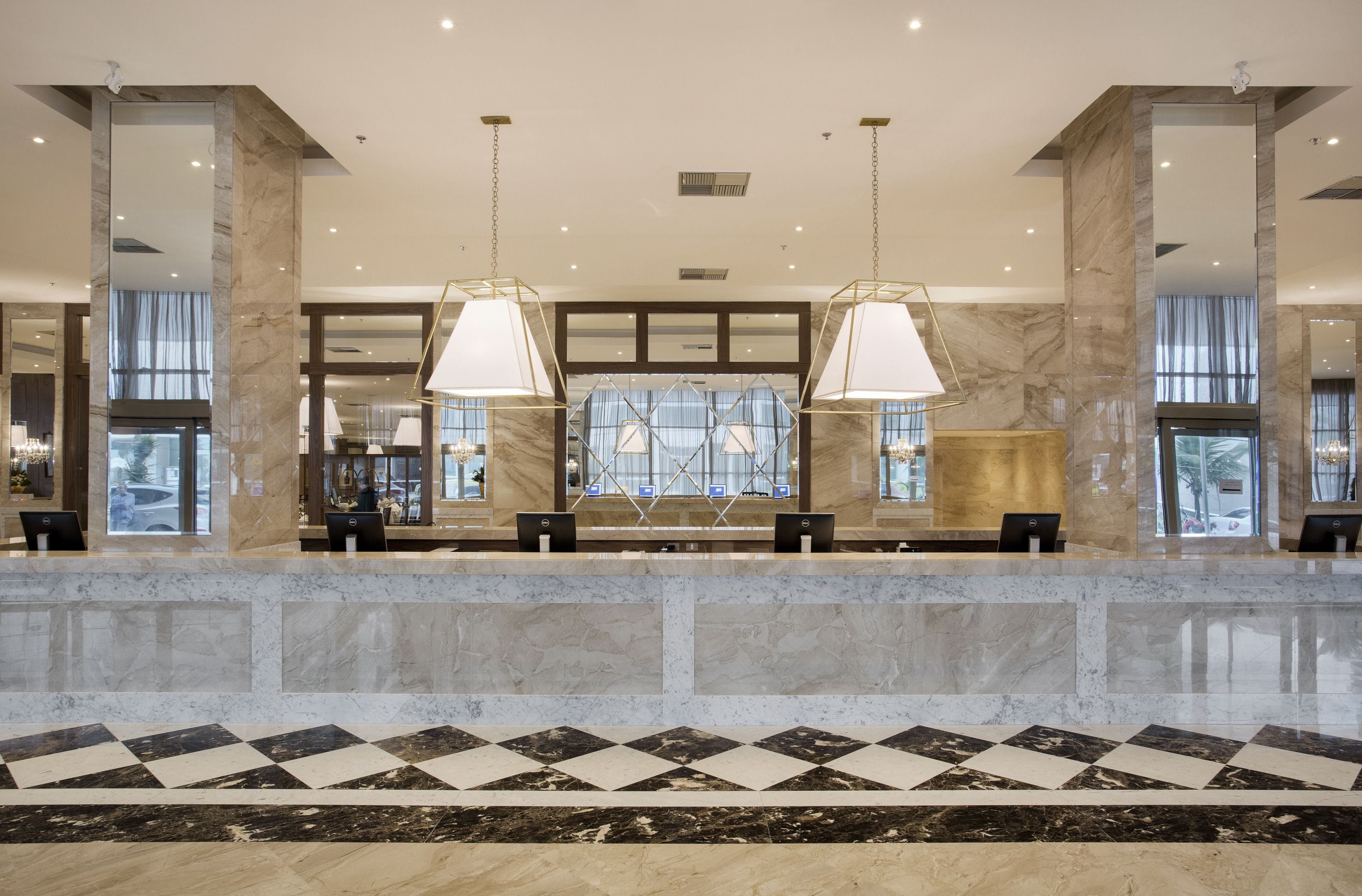 A hotel reception area with marble flooring, a check-in counter, and large windows.