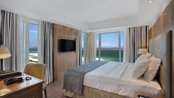 Una habitación de hotel con una cama grande, un escritorio con lámpara, televisión y vista al océano.