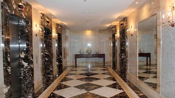 Un vestíbulo de hotel con pisos de mármol, ascensores y una mesa consola central.