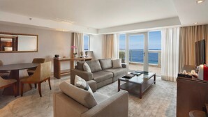 Un salón amplio con un sofá grande, una mesa de centro y un comedor con mesa y sillas. Hay un ventanal con vistas al océano.