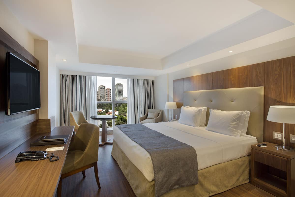 Ett modernt hotellrum med en stor säng, ett skrivbord, en TV och utsikt över staden.