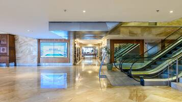 A modern hotel lobby with a marble floor, a large digital screen displaying 'Windsor', and a staircase with glass railings.