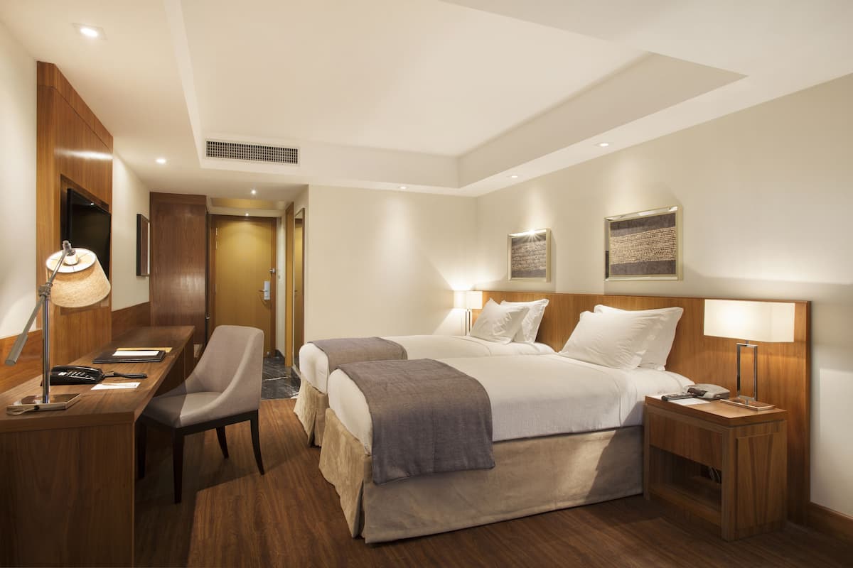 Ett hotellrum med ett skrivbord, två sängar, en stol och sänglampor.