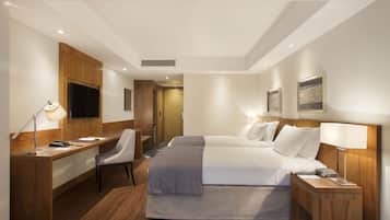 Ein Hotelzimmer mit Schreibtisch, zwei Betten, einem Sessel, einem Fernseher und Kunstwerken an den Wänden.