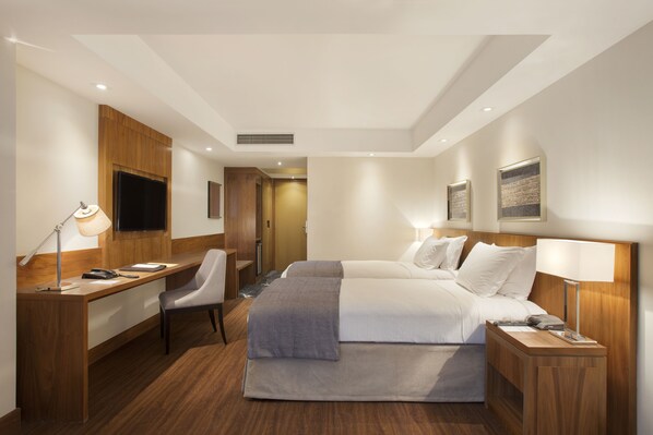 Habitación de hotel con escritorio, dos camas, una silla, televisor y obras de arte en las paredes.
