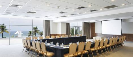 Une salle de conférence avec une longue table, des chaises, un écran de projection et une vue sur l’océan.