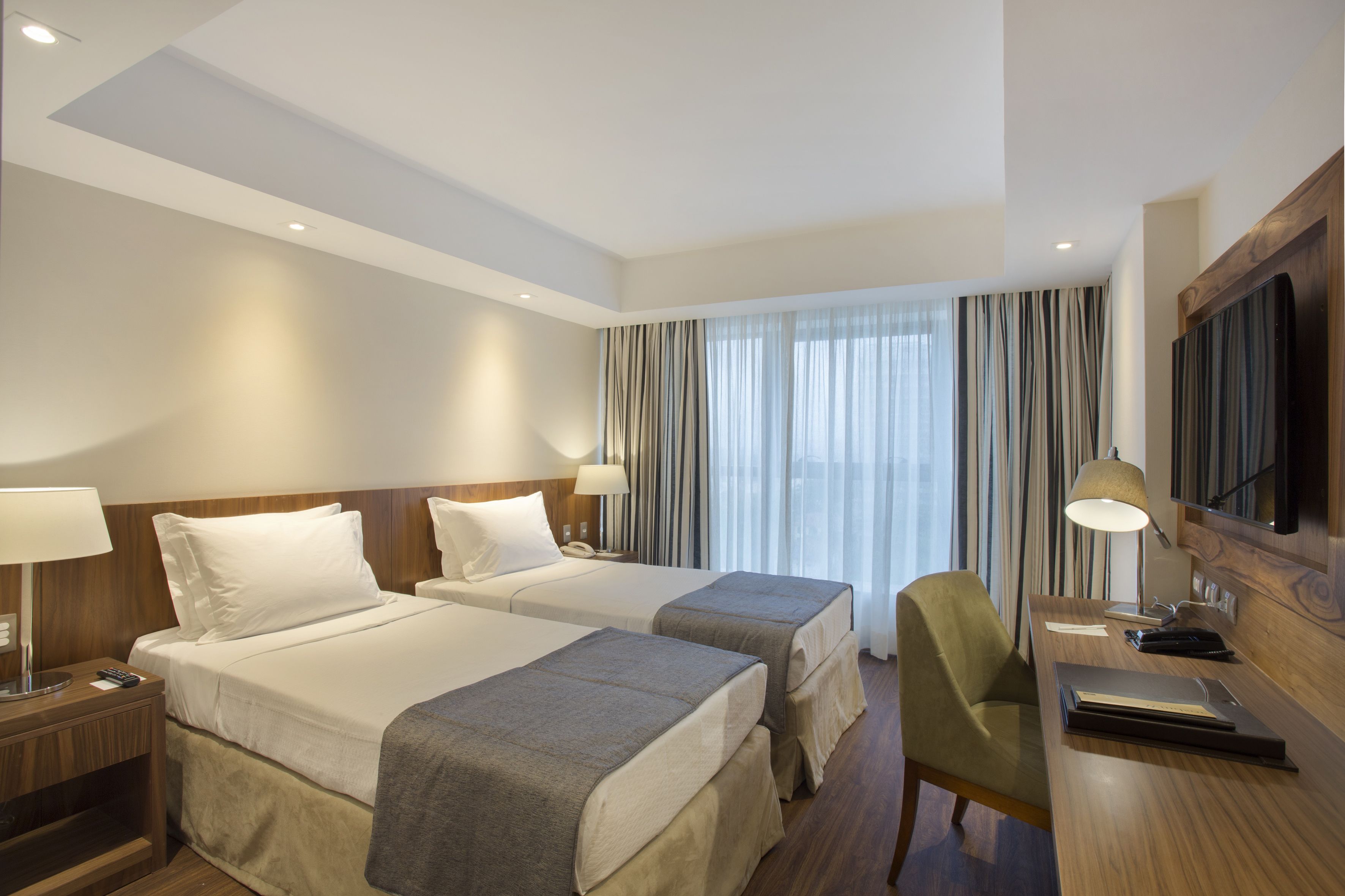 A hotel room with two beds, a desk, a chair, a TV, and a window with curtains.