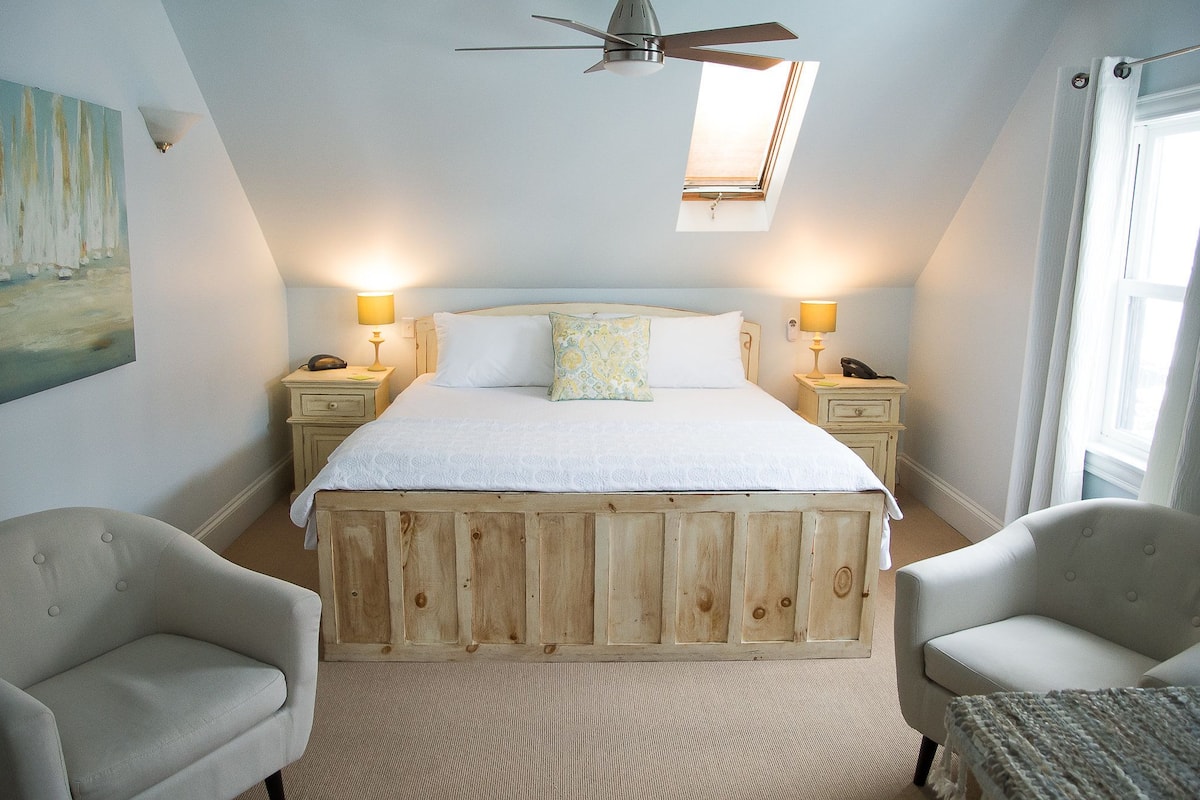 A bedroom with a wooden bed, two bedside tables with lamps, a ceiling fan, and a window with curtains.