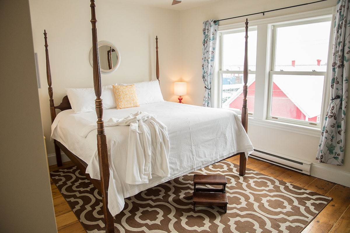 A four-poster bed with a white bedspread, a bedside lamp, and a patterned rug.