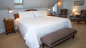 Um quarto bem organizado, com uma cama grande, luminárias de cabeceira, mesa de cabeceira de madeira, um banco e uma cadeira.