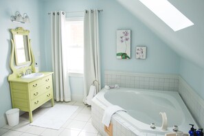 A bathroom with a bathtub, a vanity with a mirror, a window with curtains, and two wall-mounted flower paintings.
