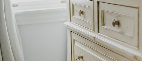 A white dresser with multiple drawers and knobs, positioned next to a window with a white curtain.