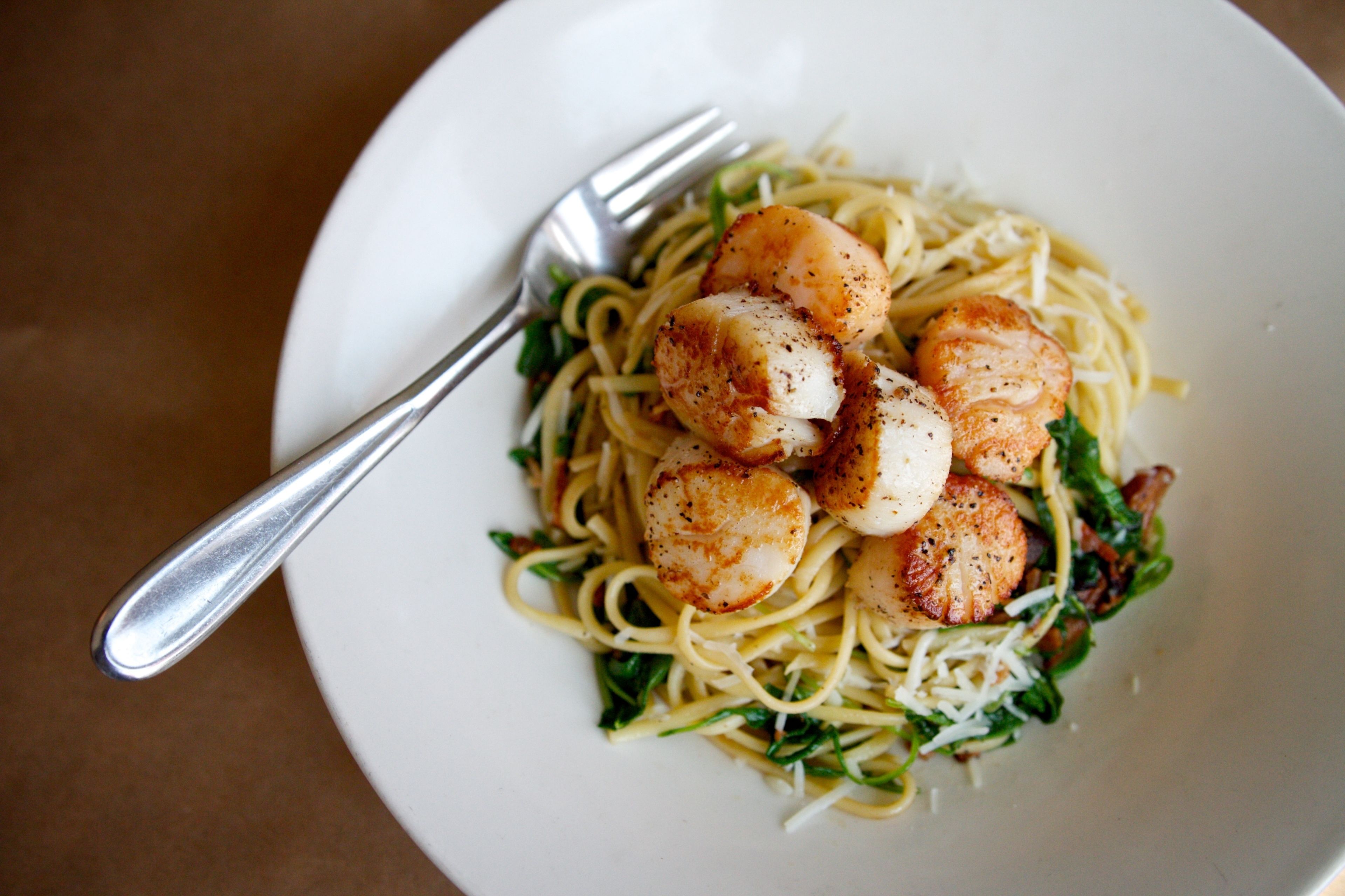 A plate of pasta with seared scallops and greens.