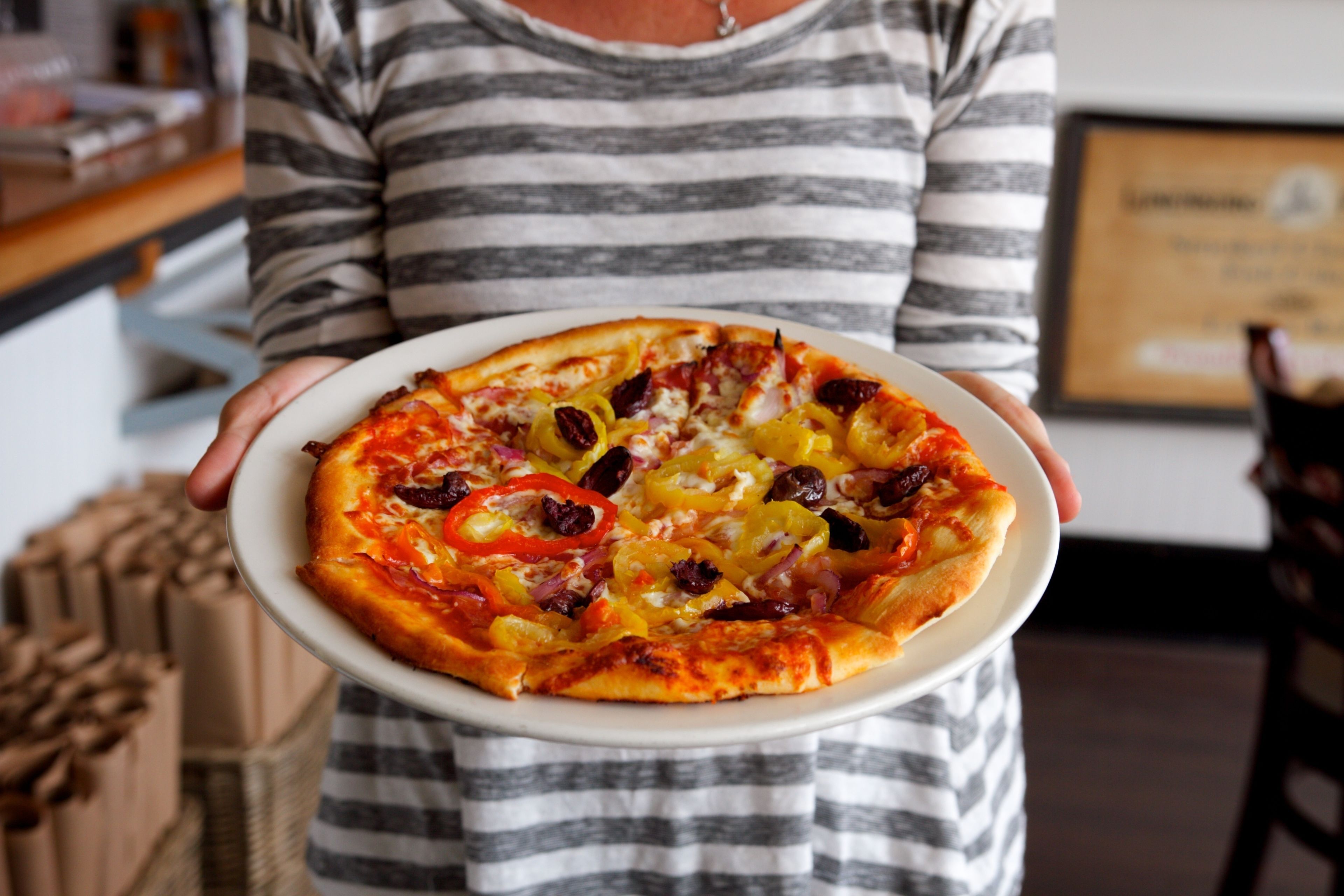 Uma pessoa segurando uma pizza com diversos ingredientes.