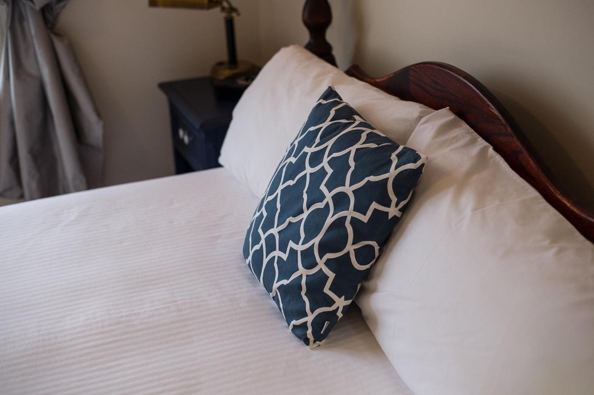 A bed with a white sheet and two pillows, one with a geometric pattern and the other plain.