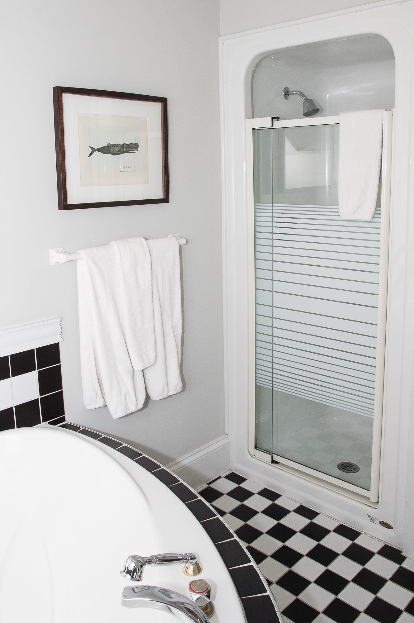 A bathroom with a bathtub, a glass-enclosed shower, a framed picture of a whale, and a checkered floor.
