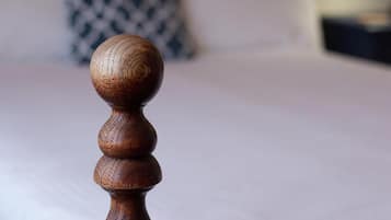 A wooden bedpost with a rounded top, a bed with white bedding, and a patterned pillow in the background.