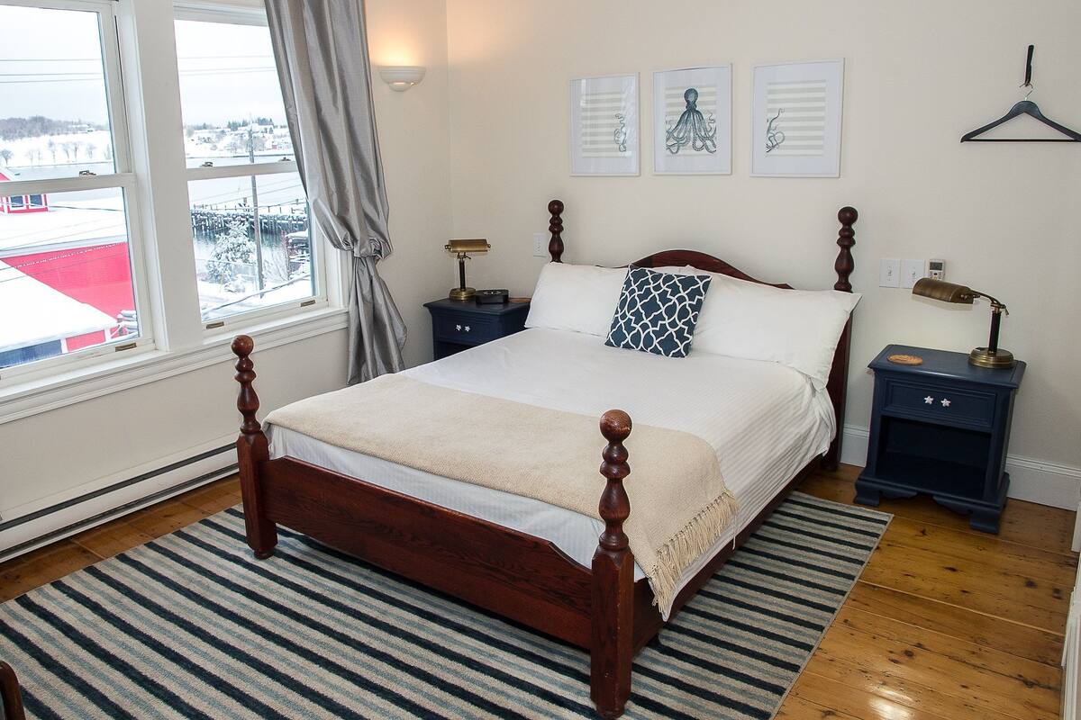 A neatly arranged bedroom with a wooden bed, a striped rug, and a view of a snowy landscape through the window.