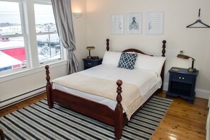 A neatly arranged bedroom with a wooden bed, a striped rug, and a view of a snowy landscape through the window.