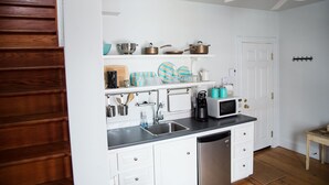 Een compacte keuken met witte kastjes, een zwart aanrecht en een ingebouwde vaatwasser. Boven de gootsteen zijn planken met verschillende keukenspullen, en een magnetron staat op het aanrecht.