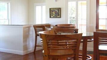 A dining area with wooden chairs and a table, a ceiling fan, and a window with blinds.
