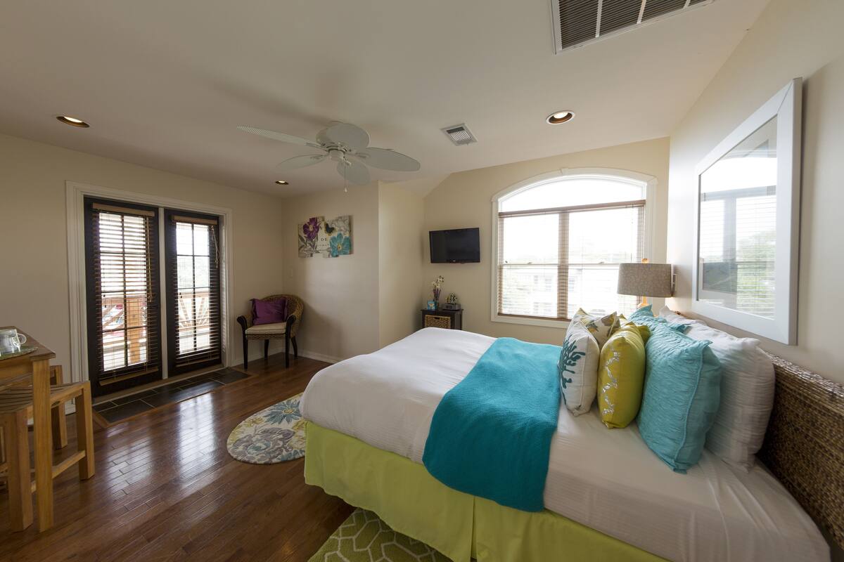 A bedroom with a bed, a ceiling fan, a TV, and a window.