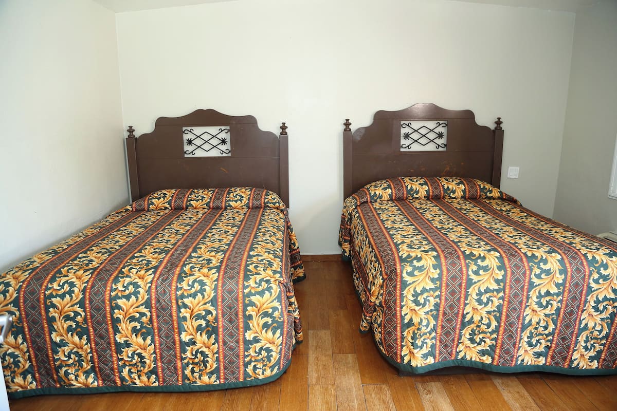 Two twin beds with ornate headboards and matching bedspreads in a room with wooden flooring and white walls.