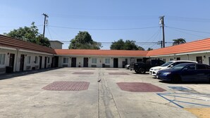 A motel with a row of rooms, a parking lot, and a clear blue sky. - The Fly Inn (Lynwood)